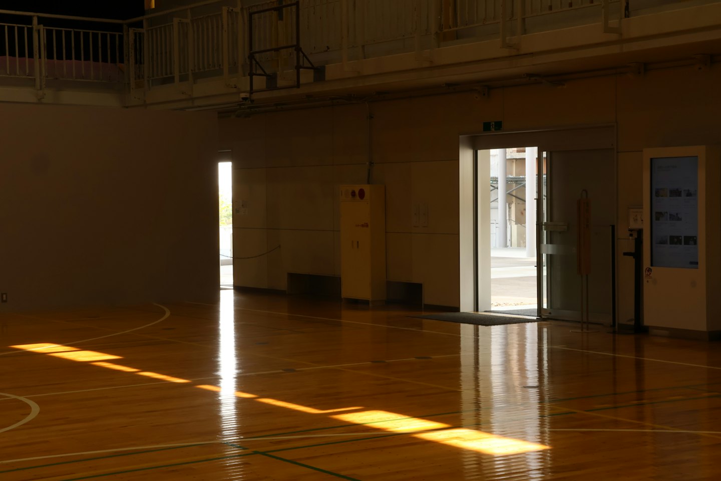 Solstrålar strömmar genom dörröppningar in på ett tomt gymgolv av trä.